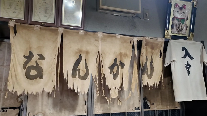 創業当時に使われていた暖簾と、店主ご自身でつくった「入曽Tシャツ」