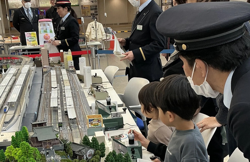 Nゲージを体験する電車好きの子供(こども)と補助する駅員