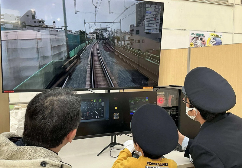 トレインシミュレーターを体験する親子とJR職員の様子
