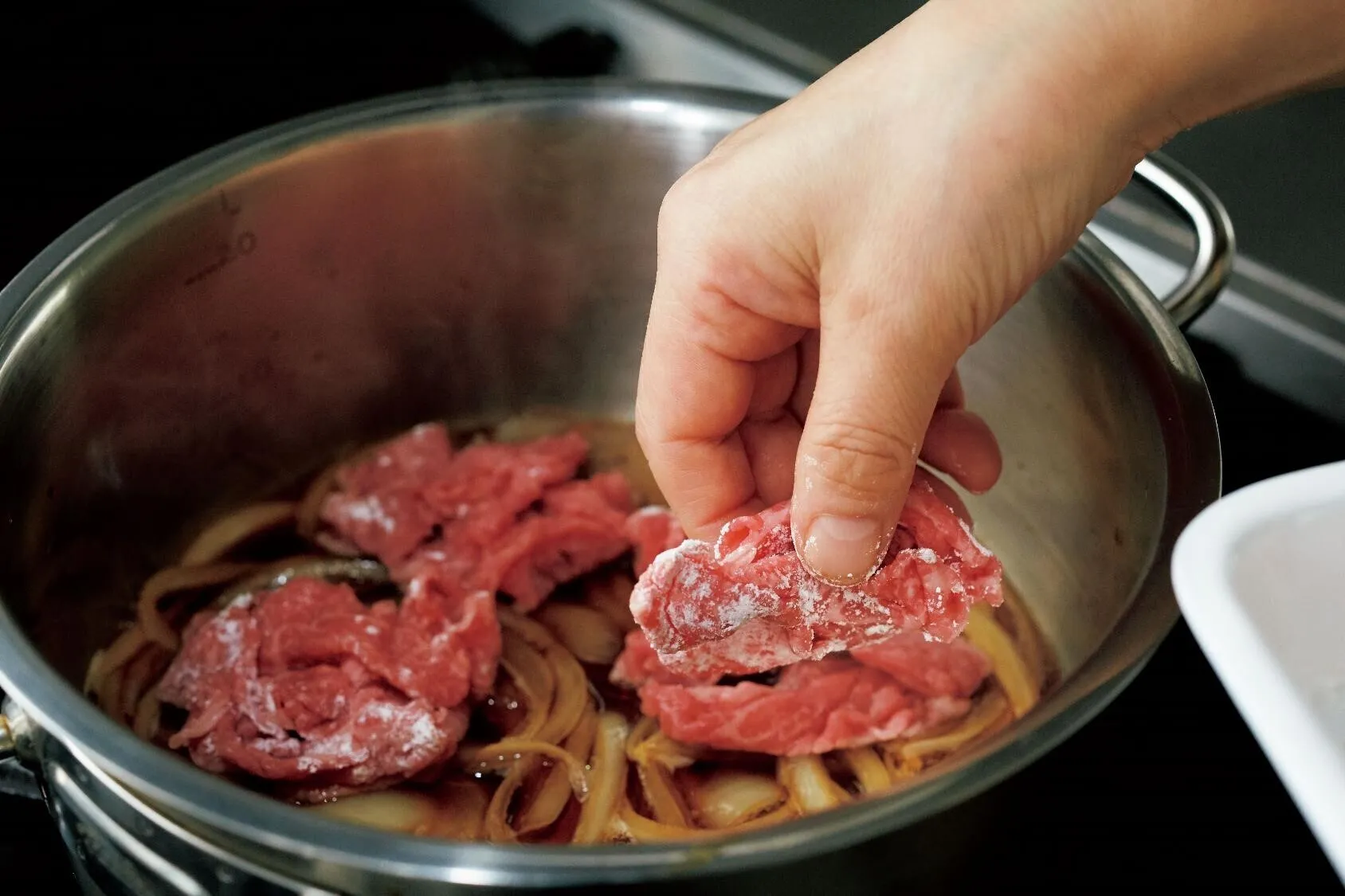 口径20cmの鍋（またはフライパン）にAの材料を入れ、中火にかける。煮立ったら玉ねぎを加えて弱火にし、5分ほど煮る。牛肉を粉の面を下にして入れ、さわらずに1分ほど煮る。上下を返し、さらに1分ほど煮て火を止める。

（画像：牛肉を粉の面を下にして入れる。）
