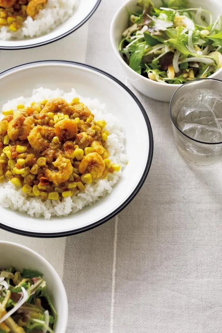 フライパンにバターを中火で熱してエビを炒め、色が変わったら白ワインをふって取り出す。フライパンをさっと拭き、オリーブオイルを中火で熱し、玉ねぎを炒める。しんなりしたらとうもろこしを加え、カレー粉をふってさっと炒める。トマト、水1/2カップを加えて煮立て、塩を加える。ふたをして弱めの中火で5～6分煮てエビを戻し入れ、ひと煮する。器にご飯を等分に盛り、カレーを1/2量ずつかける。