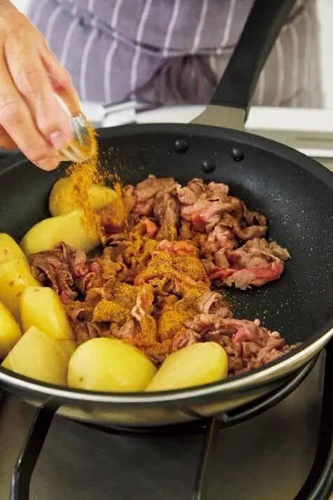 じゃがいもは皮をむいて大きめの一口大に切る。フライパンにバターを中火で溶かし、じゃがいもを2～3分炒める。まわりが透き通ってきたら牛肉を加えて炒め、肉の色が変わったらカレー粉を加えて炒める。

（画像：カレー粉を加える）