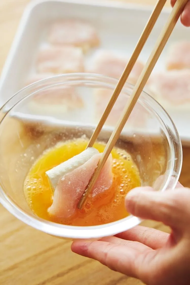 フライパンにオリーブオイルを中火で熱し、鶏肉と豆腐を1切れずつ組み合わせて、卵液をからめながら入れる。焼き色がついたら返し、色が変わったら再び卵液をからめて並べ入れる。ふたをして弱火で両面を2～3分ずつ焼く。

（画像：鶏肉と豆腐に卵液をからめる。）