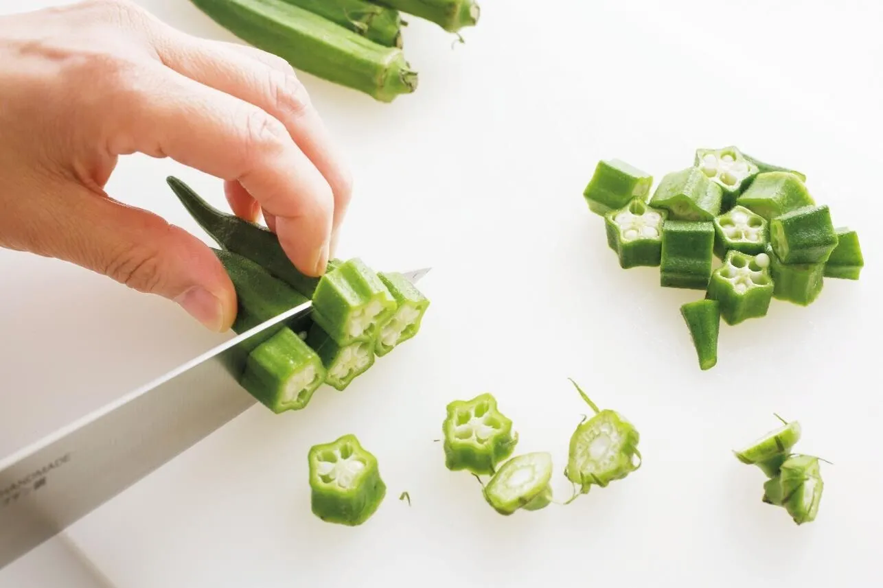 豆腐は1.5cm角に切る。オクラはへたを切り、幅1cmの輪切りにする。ねぎ、にんにくはともにみじん切りにする。

（画像：オクラを輪切りにする。）