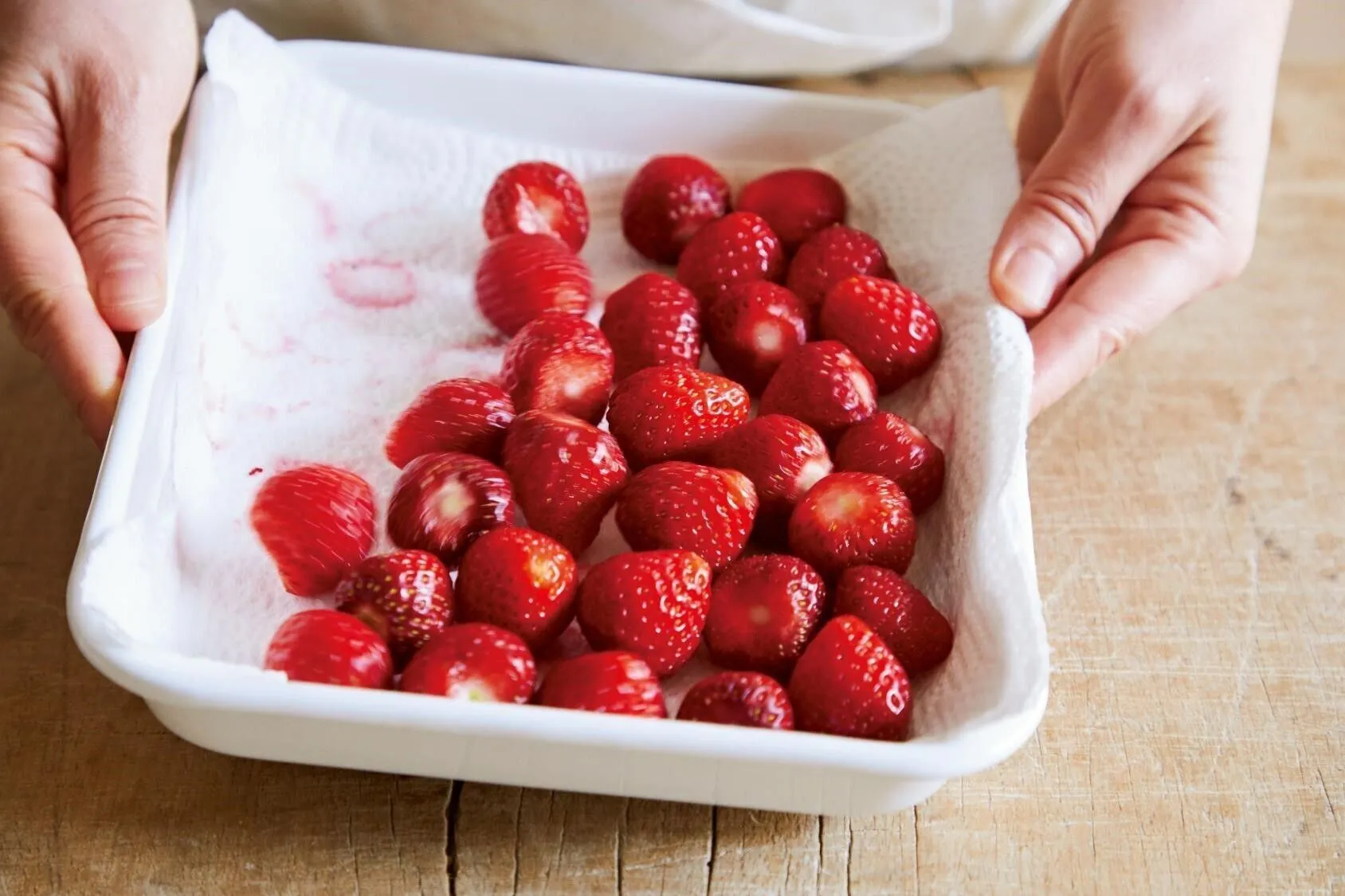 大きめのバット（または盆ざる）にペーパータオルを二重にして敷く。いちごは洗ってからへたを切り、バットに入れる。バットを左右に揺らしていちごをころがし、水けを取る（こうすると、一つ一つ拭かなくていいのでラク）。

（画像：バットを左右に揺らす。）